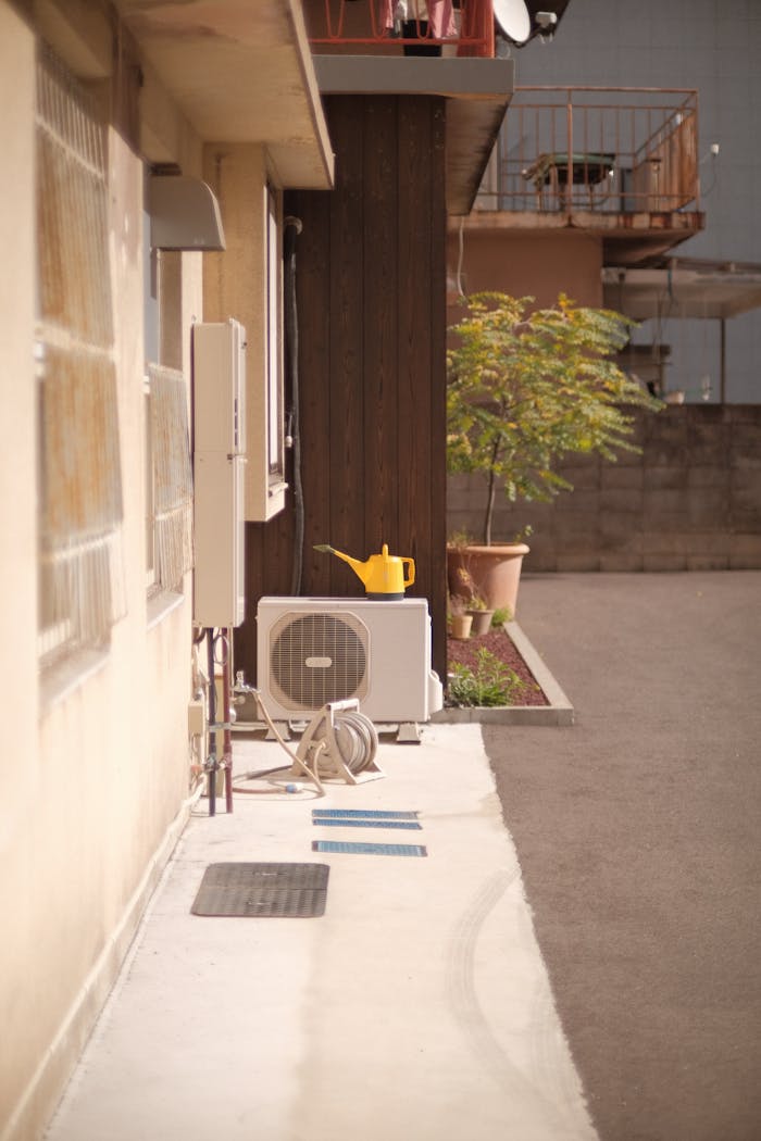 A quiet apartment scene featuring an outdoor air conditioning unit and a yellow watering can.